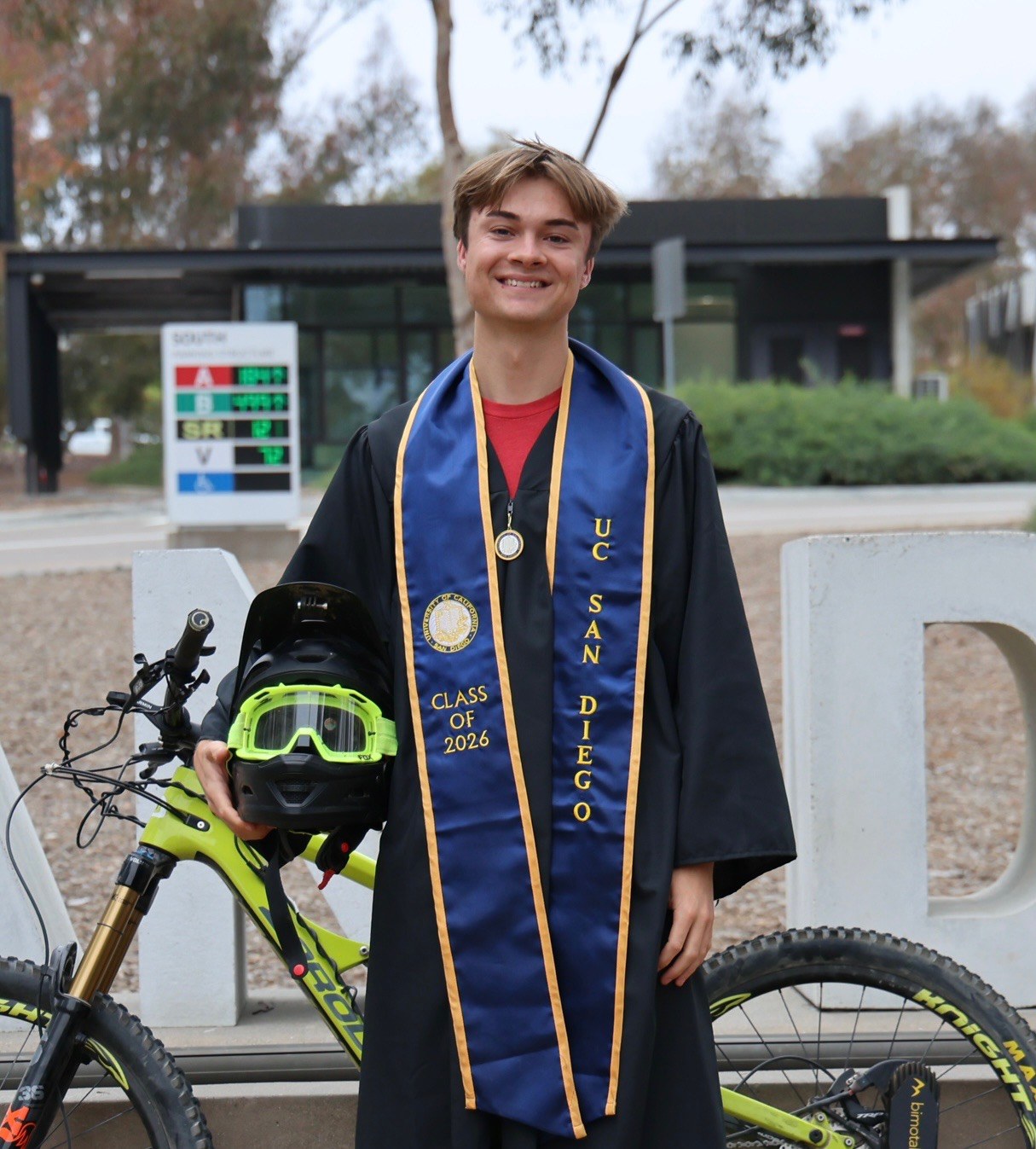Will Diego in UC San Diego graduation regalia holding a bike helmet